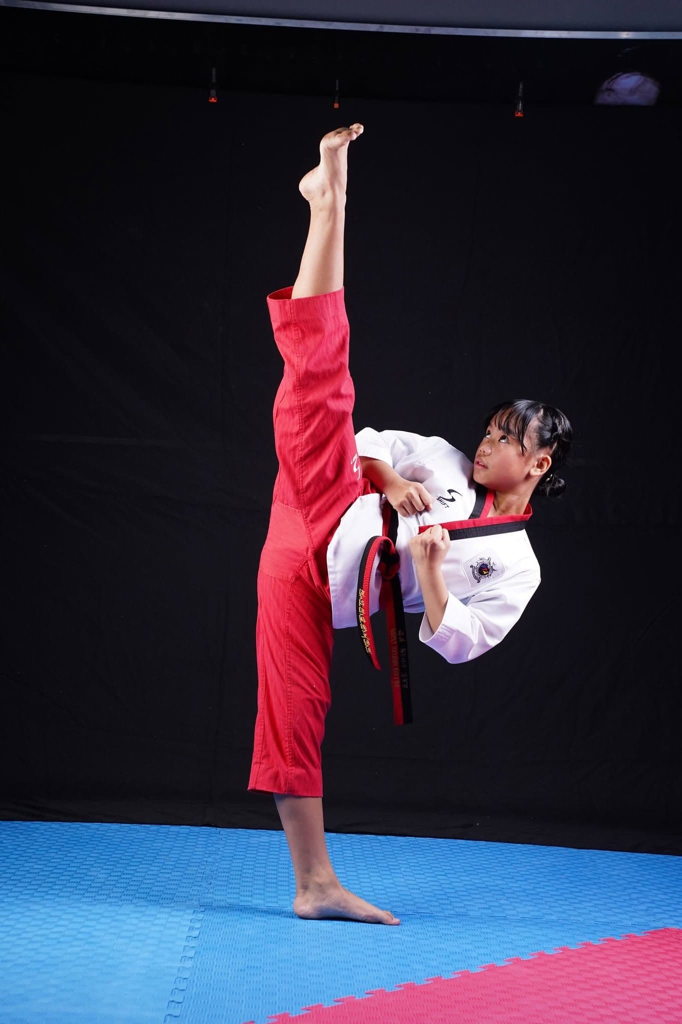 A young WVT student holding a high kick above her head.