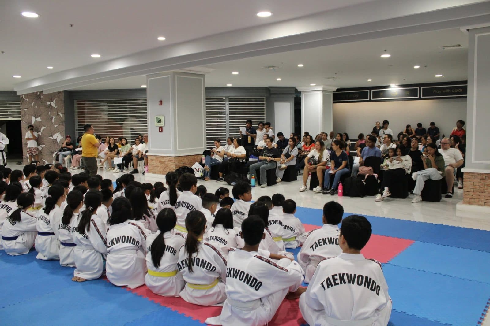 WVT students seated in rows on the mat at an indoor event.
