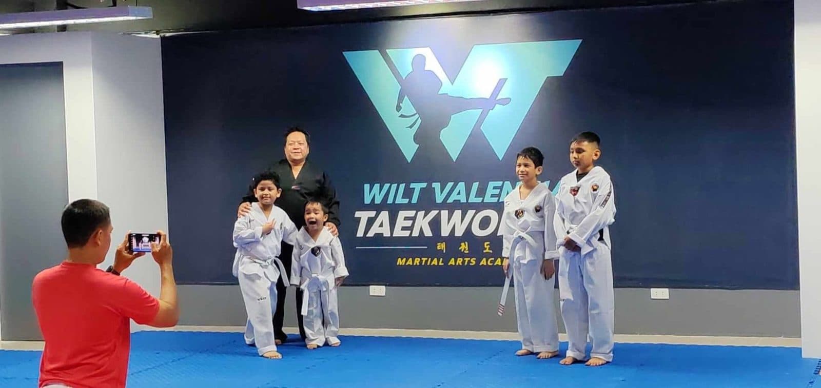 Young WVT students posing in front of the Wilt Valencia Taekwondo backdrop.