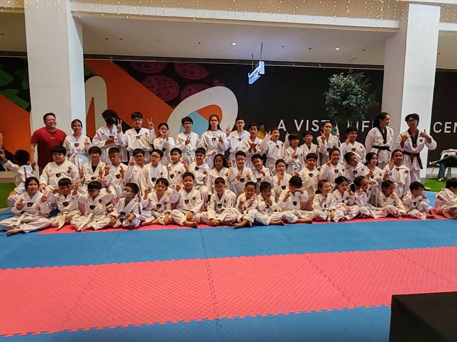 A large group of WVT students in white uniforms seated together on the mat at the NOMO Vista branch.