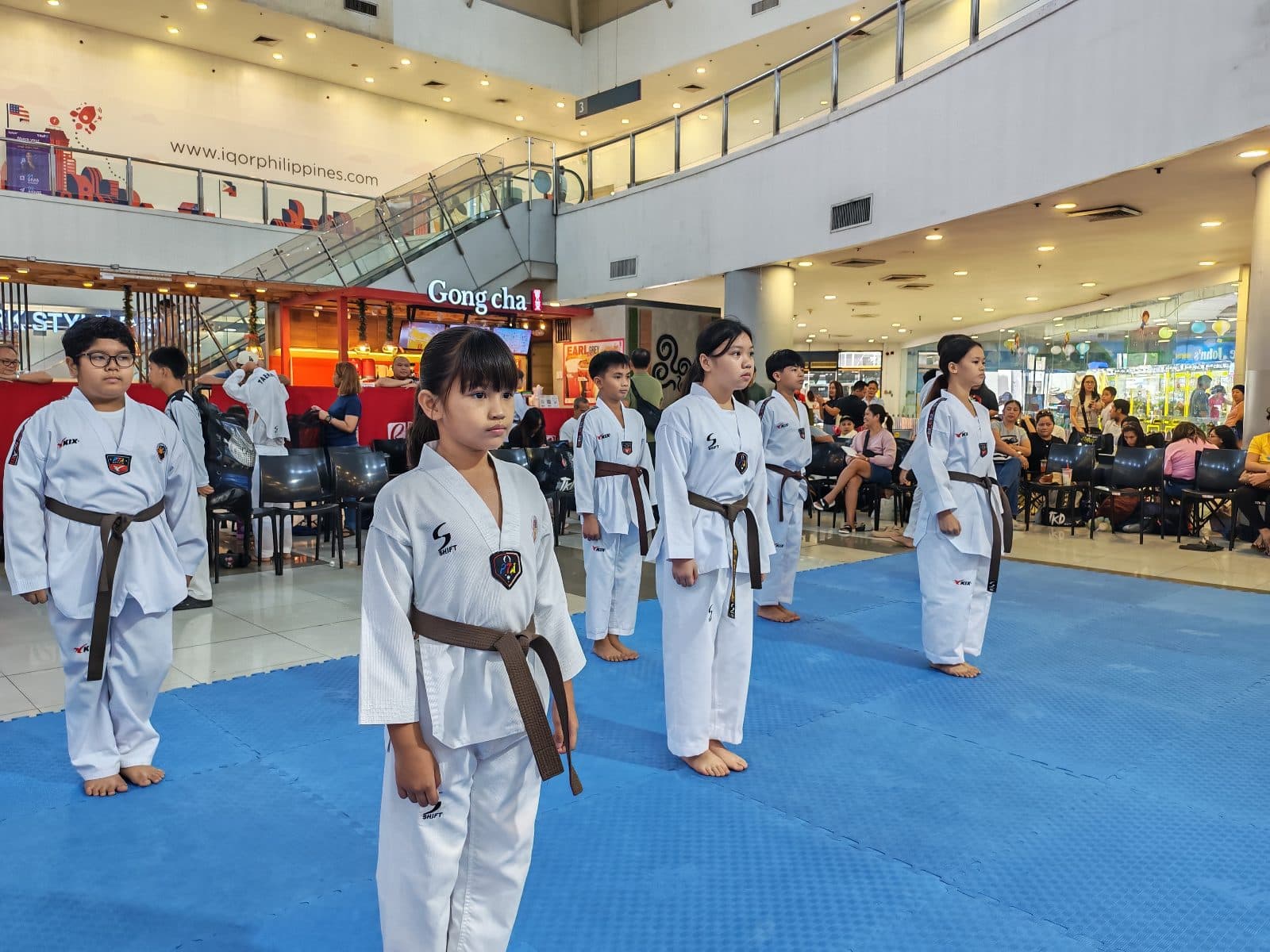 WVT students performing poomsae together on blue mats at a mall event.